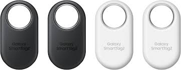 Four Galaxy SmartTags in black and white on a white background. Front view of the Samsung Galaxy SmartTag2 Bluetooth tracker, showcasing its redesigned pill-shaped white casing with a large premium metal-lined cutout loop on a clean background.